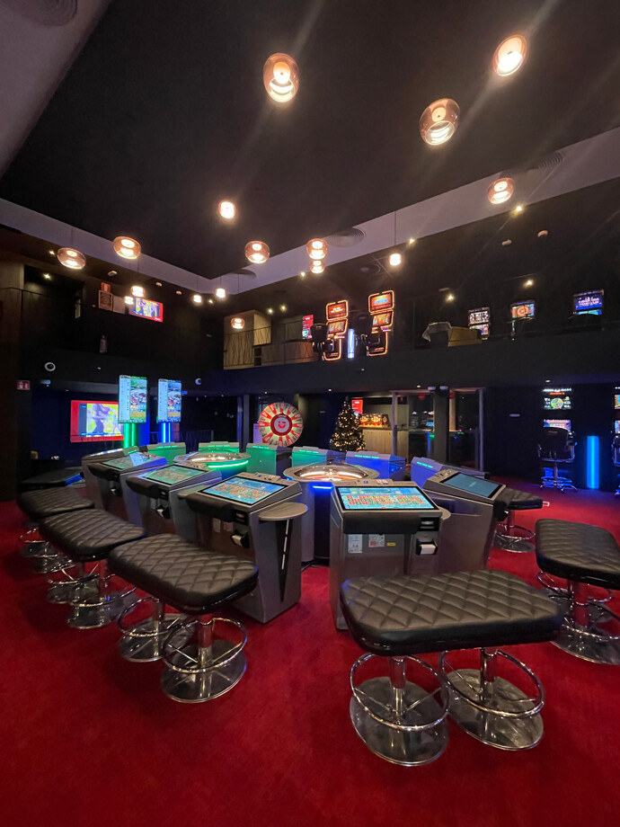 Une salle de jeux du casino d'Arlon avec des tables de roulette électronique entourées de sièges noirs rembourrés.